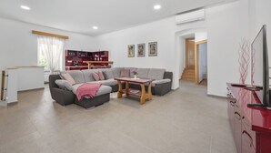 A modern living room with a sectional sofa, a wooden coffee table, and a red cabinet with a TV. - Stone Gem - Villa Katarina with Private Pool (Nedešcina)
