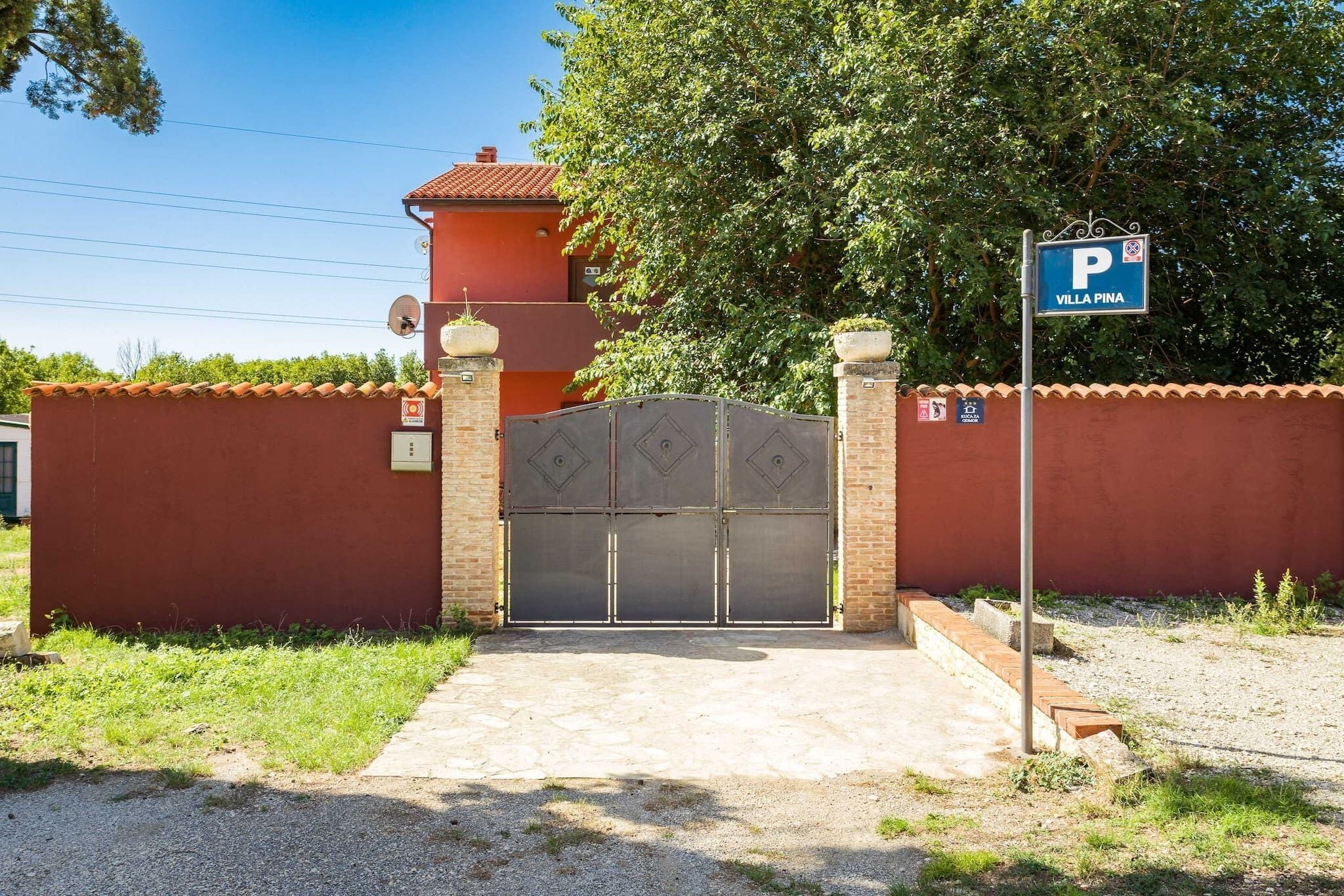 A gated entrance to a property named Villa Pina, featuring a metal gate and a parking sign.