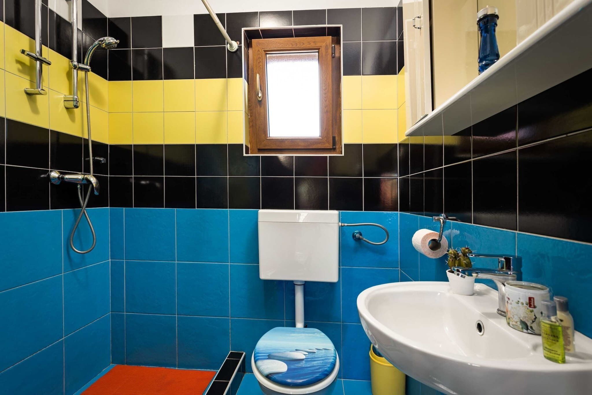 Une salle de bain avec des carreaux bleus et jaunes, un lavabo blanc et des toilettes avec un abattant bleu.