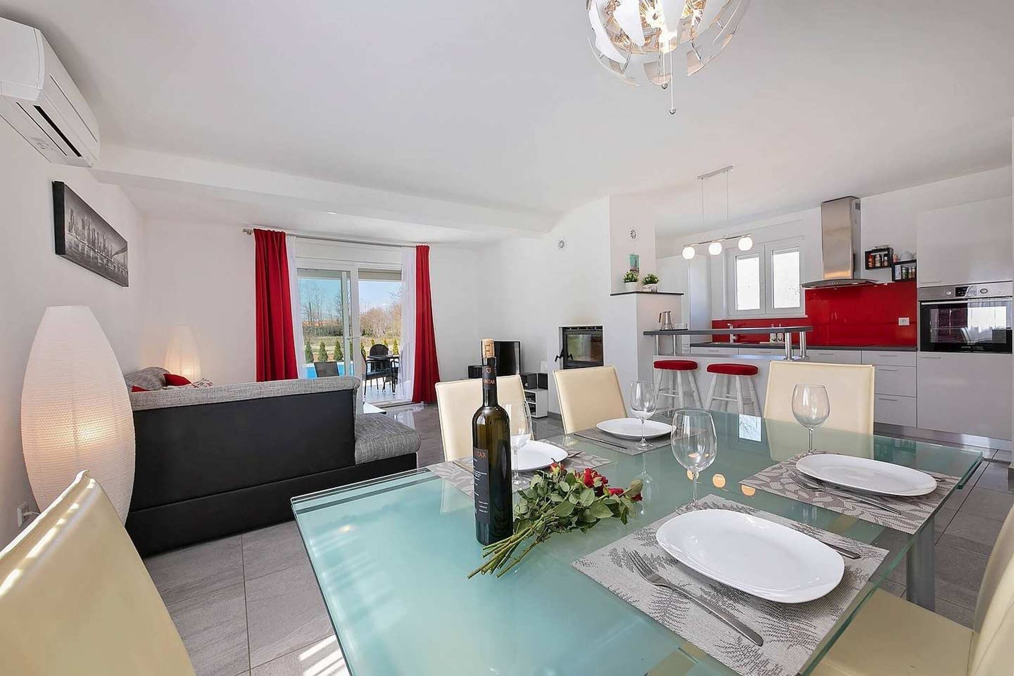 A modern dining area with a glass table, red curtains, and a kitchen in the background.