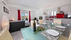 A modern dining area with a glass table, red curtains, and a kitchen in the background. - Villa Sofia with Private Pool (Santalezi)
