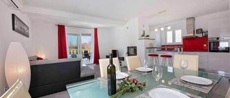 A modern dining area with a glass table, red curtains, and a kitchen in the background.