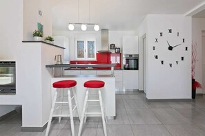 Una cocina moderna con armarios blancos, encimera roja y dos taburetes blancos con cojines rojos.