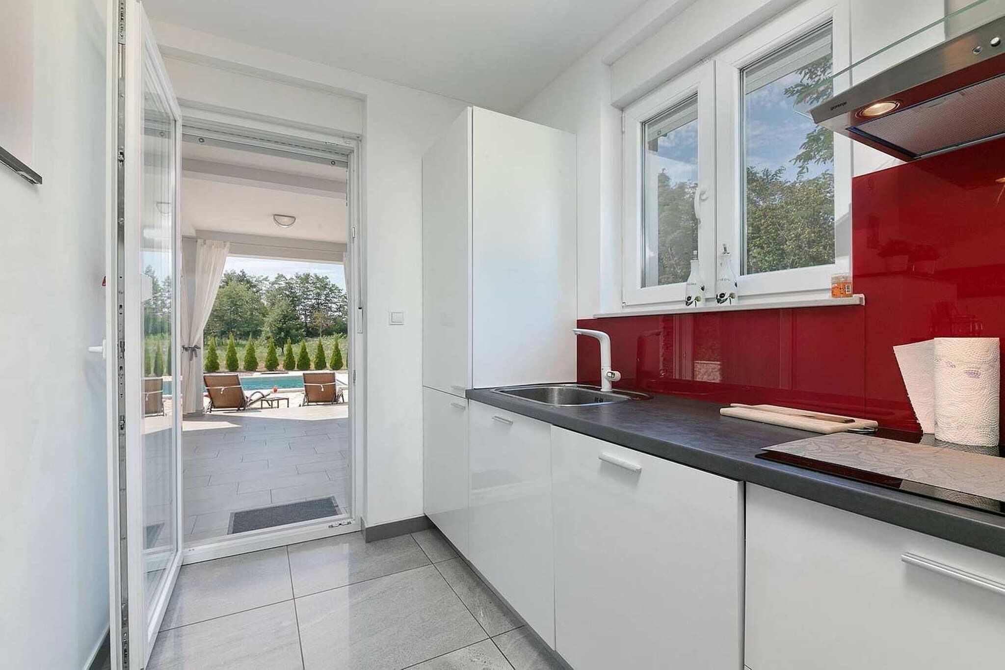 Une cuisine moderne avec des meubles blancs, un pare-feu rouge et une grande fenêtre.