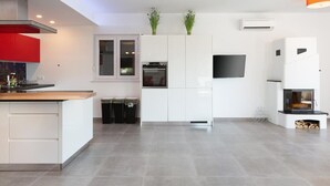 A modern kitchen with white cabinetry, a central island, a built-in oven, and a flat-screen TV.