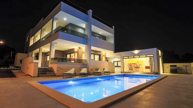 A modern two-story building with a swimming pool, outdoor seating, and a bar area.