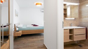 A modern bedroom with a bed, bedside table, and a nightstand. The room has a wooden floor and a white wall.
