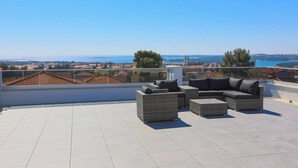 A rooftop terrace with outdoor furniture and a view of the city and sea.