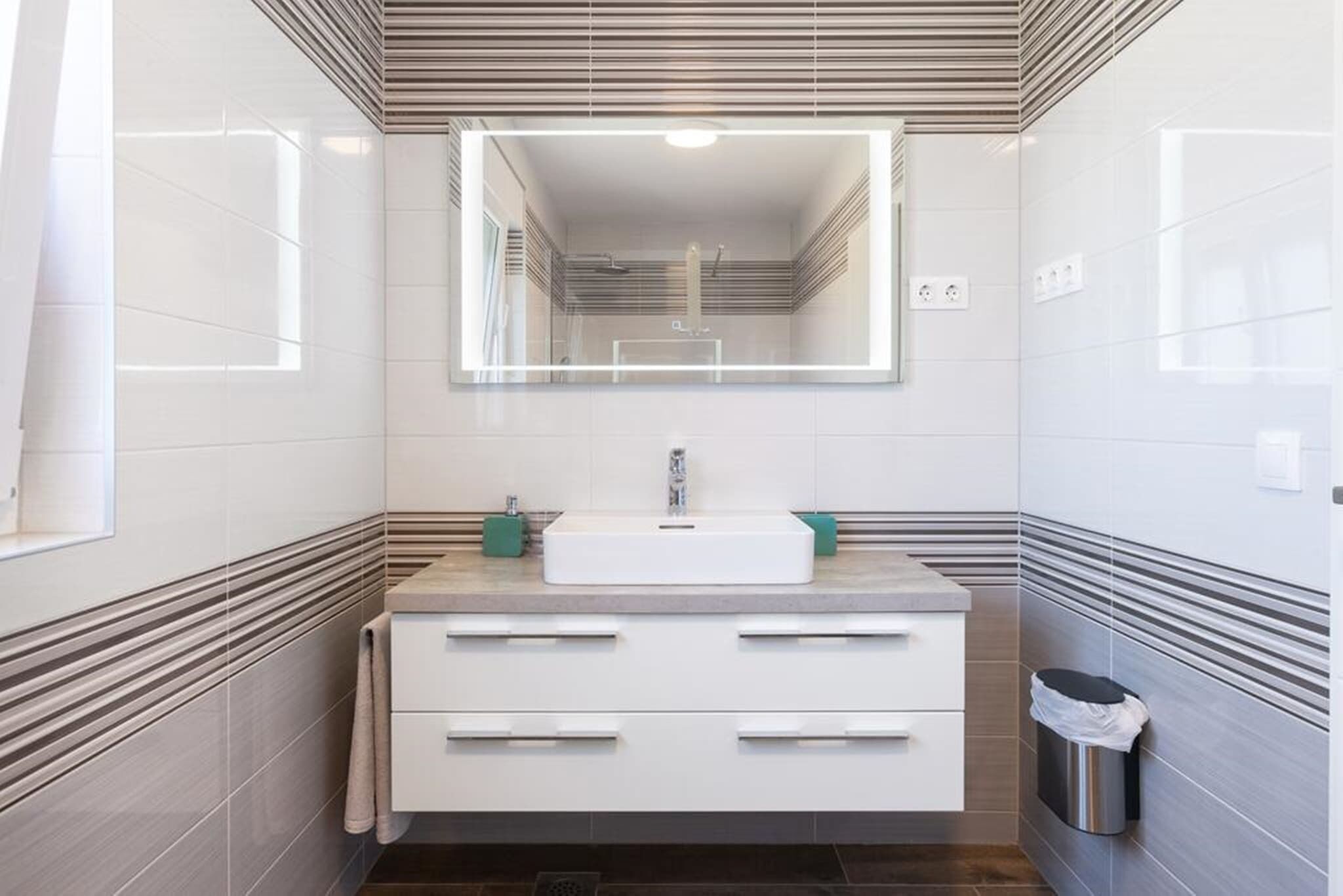 Un bagno moderno con uno specchio grande, un mobile lavabo bianco e un cestino.
