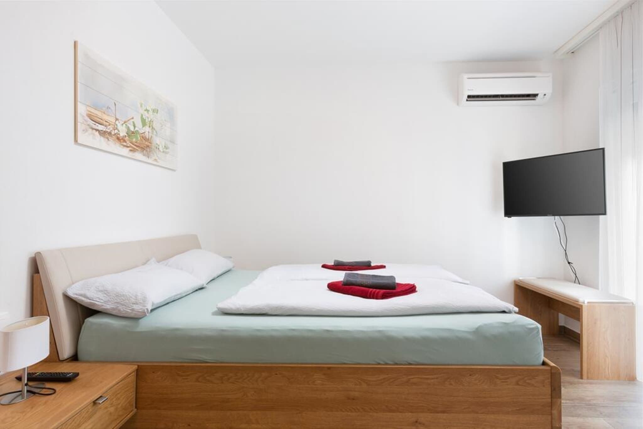 A modern hotel room with a bed, a bedside table, a TV, and an air conditioning unit.