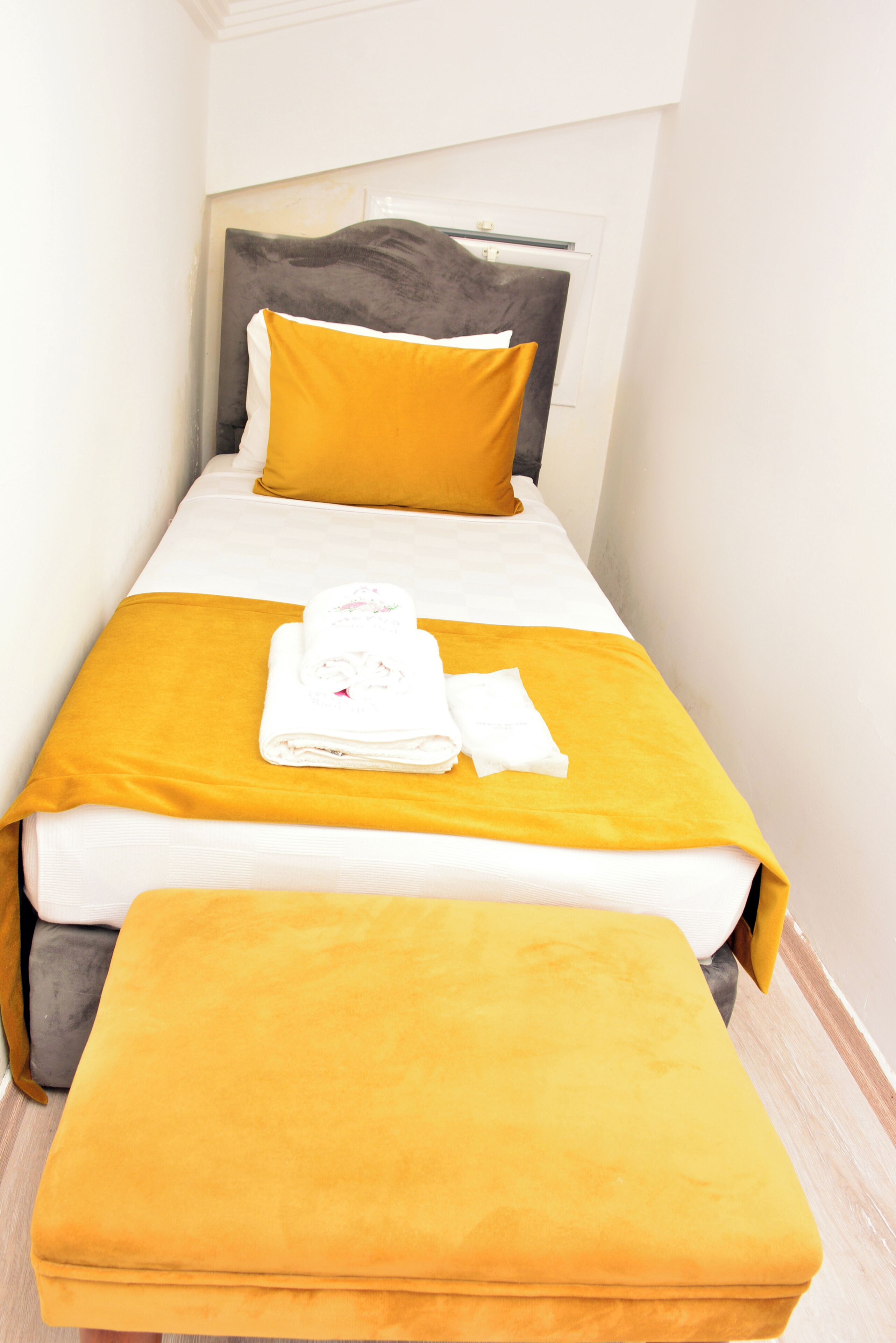 A single bed with a headboard, a bench at the foot of the bed, and a yellow bedspread.