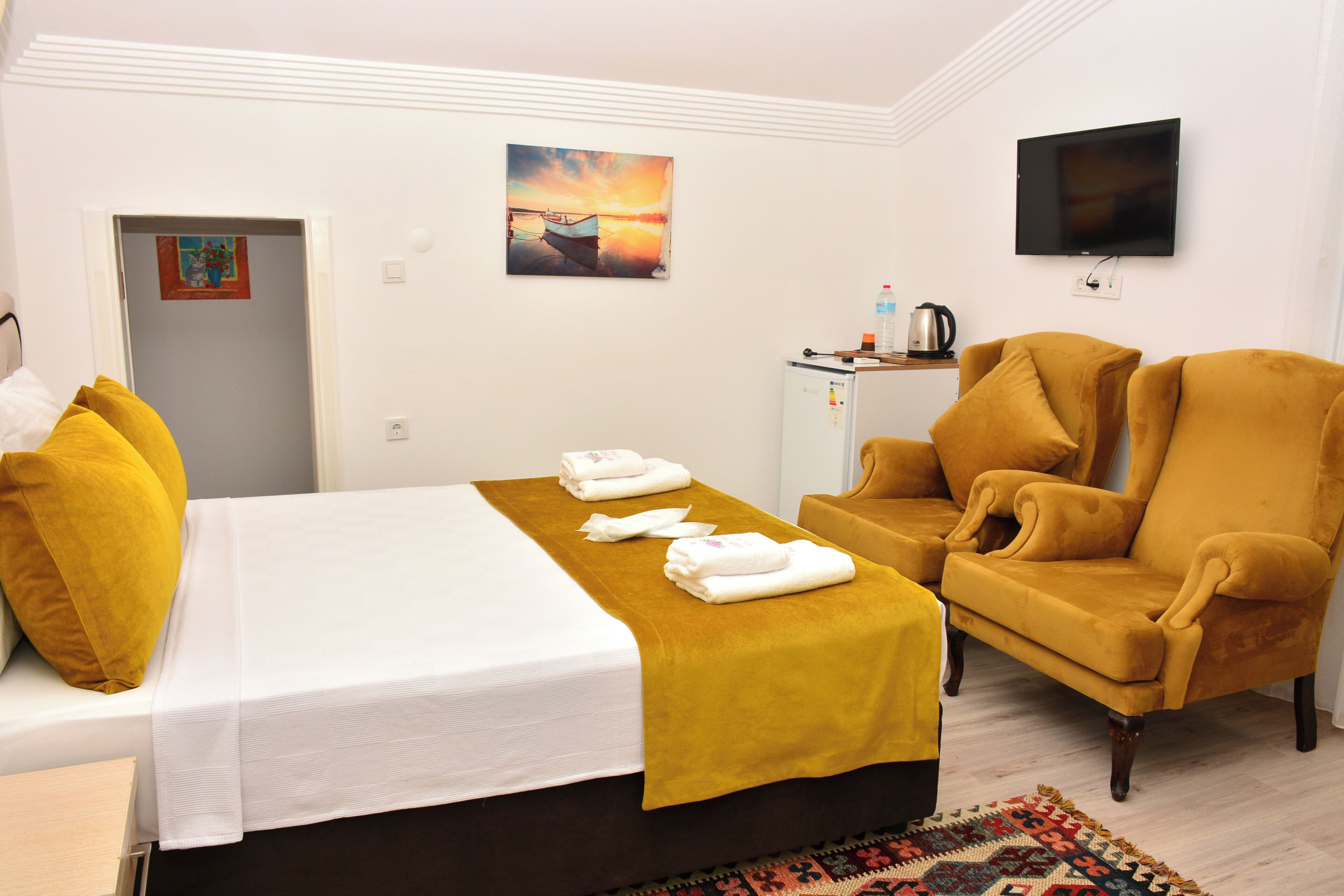 A hotel room with a bed, a sofa, a television, and a small table with a kettle.