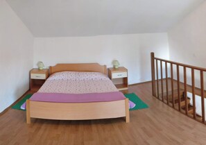 A bedroom with a wooden bed, two bedside tables with lamps, a wooden railing, and a green mat on the floor.