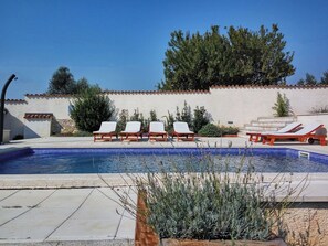 A swimming pool with lounge chairs, a stone wall, and a clear sky.