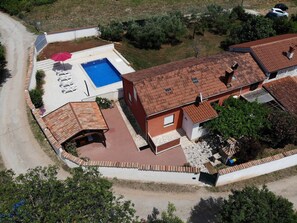 A residential property with a swimming pool, a covered patio, and a red-roofed house.