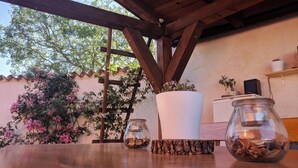 Een houten tuintafel met twee glazen potten, een witte plantenbak, en een houten klimrek met bloeiende planten.