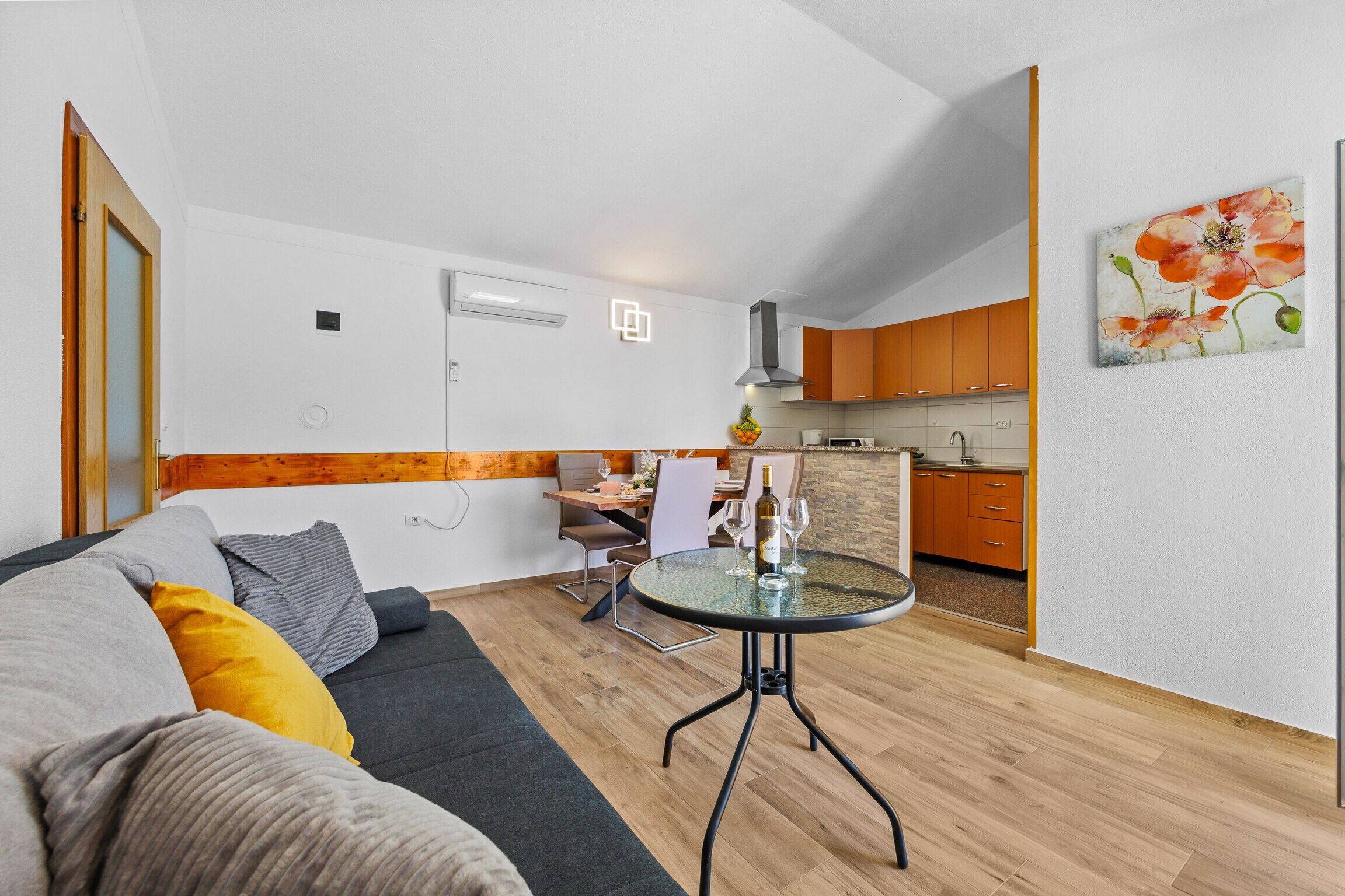 Una sala moderna con un sofá, una mesa de vidrio y una cocina al fondo.