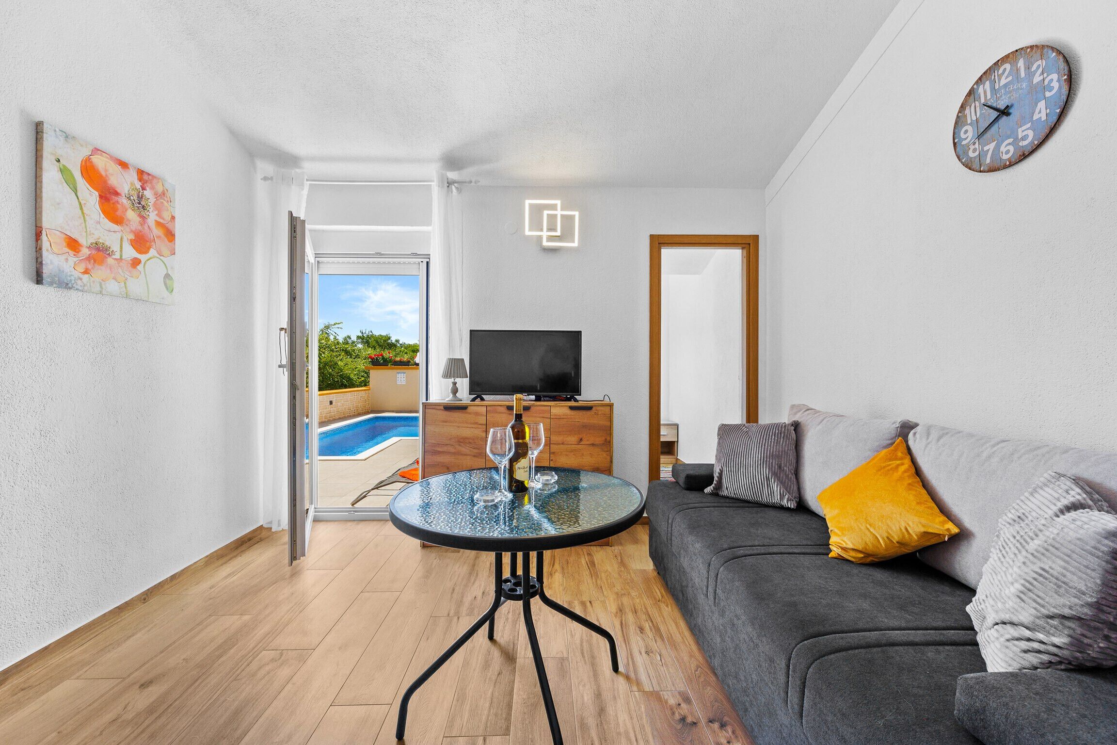 Un salon moderne avec une table en verre, un canapé gris et un téléviseur posé sur un meuble en bois.