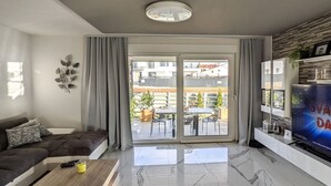 En moderne stue med sofa, sofabord, fjernsyn og en skydedør til en udendørs terrasse.