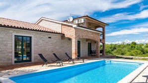 A swimming pool with lounge chairs, a brick building with a balcony, and a clear blue sky. - Villa Boris with Private Pool (Vodnjan)