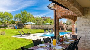 An outdoor patio with a dining table set for four, a pool, and a brick archway. - Villa Boris with Private Pool (Vodnjan)