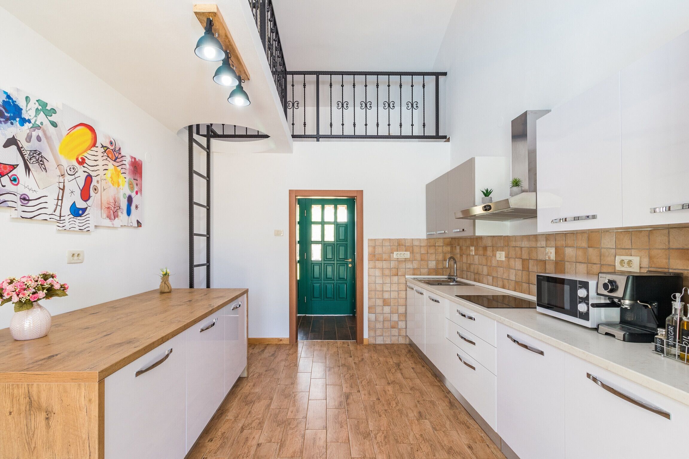 A modern kitchen with white cabinets, a wooden countertop, a green door, and a tiled backsplash.