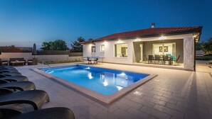 A swimming pool with lounge chairs, a covered patio, and a building with a red roof. - Holiday Home Greta with Private Pool (Salakovci)