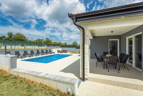 A swimming pool with lounge chairs, a dining area with tables and chairs, and a covered patio. - Holiday Home Greta with Private Pool (Salakovci)