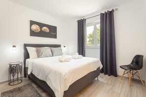 A neatly made bed with white linens and rolled towels, a black chair, a small side table, and a window with dark curtains. - Holiday Home Greta with Private Pool (Salakovci)