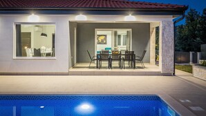 A modern house with a swimming pool, a dining area with chairs and a table, and a large window overlooking the pool. - Holiday Home Greta with Private Pool (Salakovci)