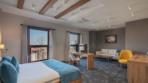Quarto de hotel com cama, escrivaninha, sofá e televisão.