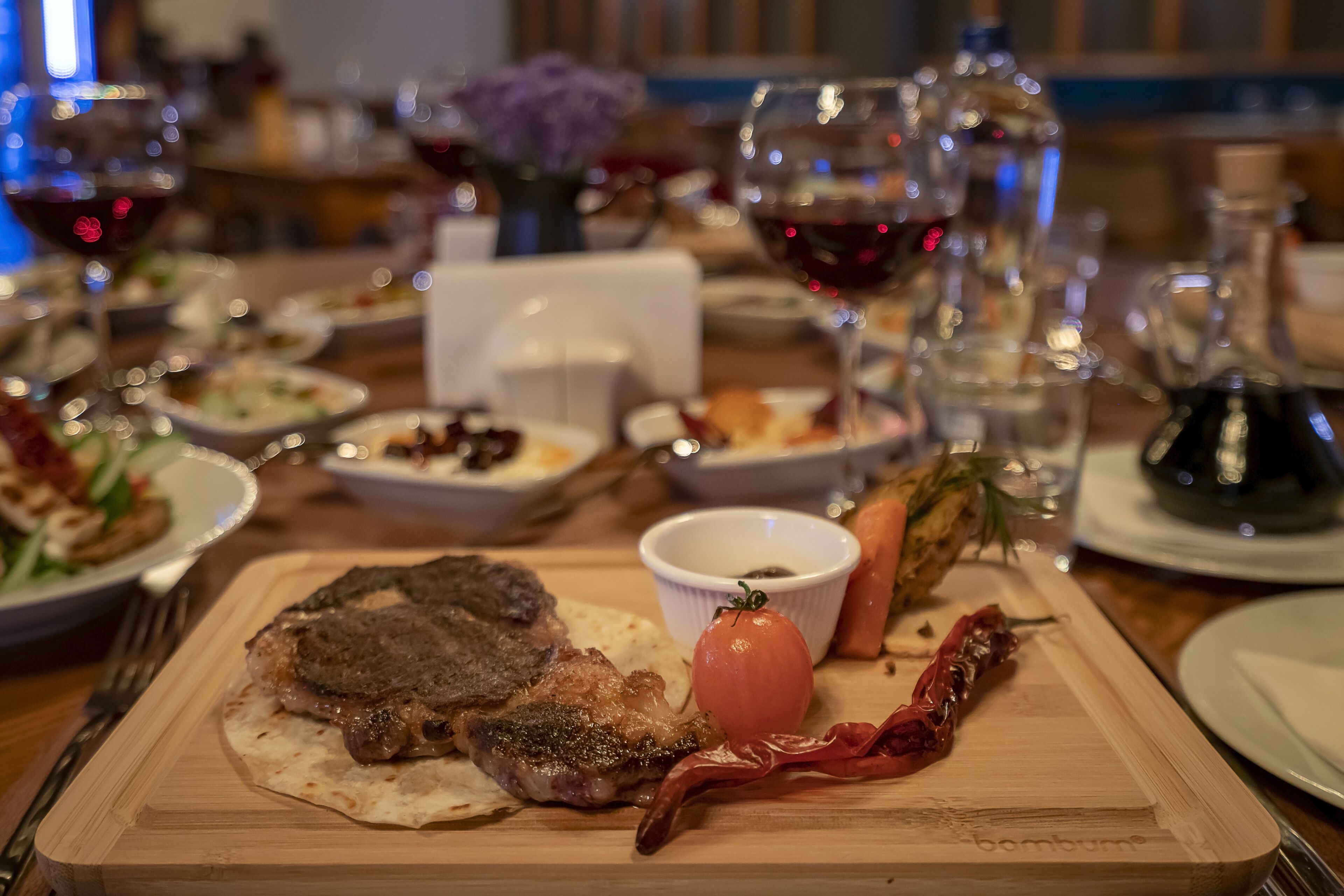 A dining table with a steak, a tomato, and a chili pepper on a wooden board.