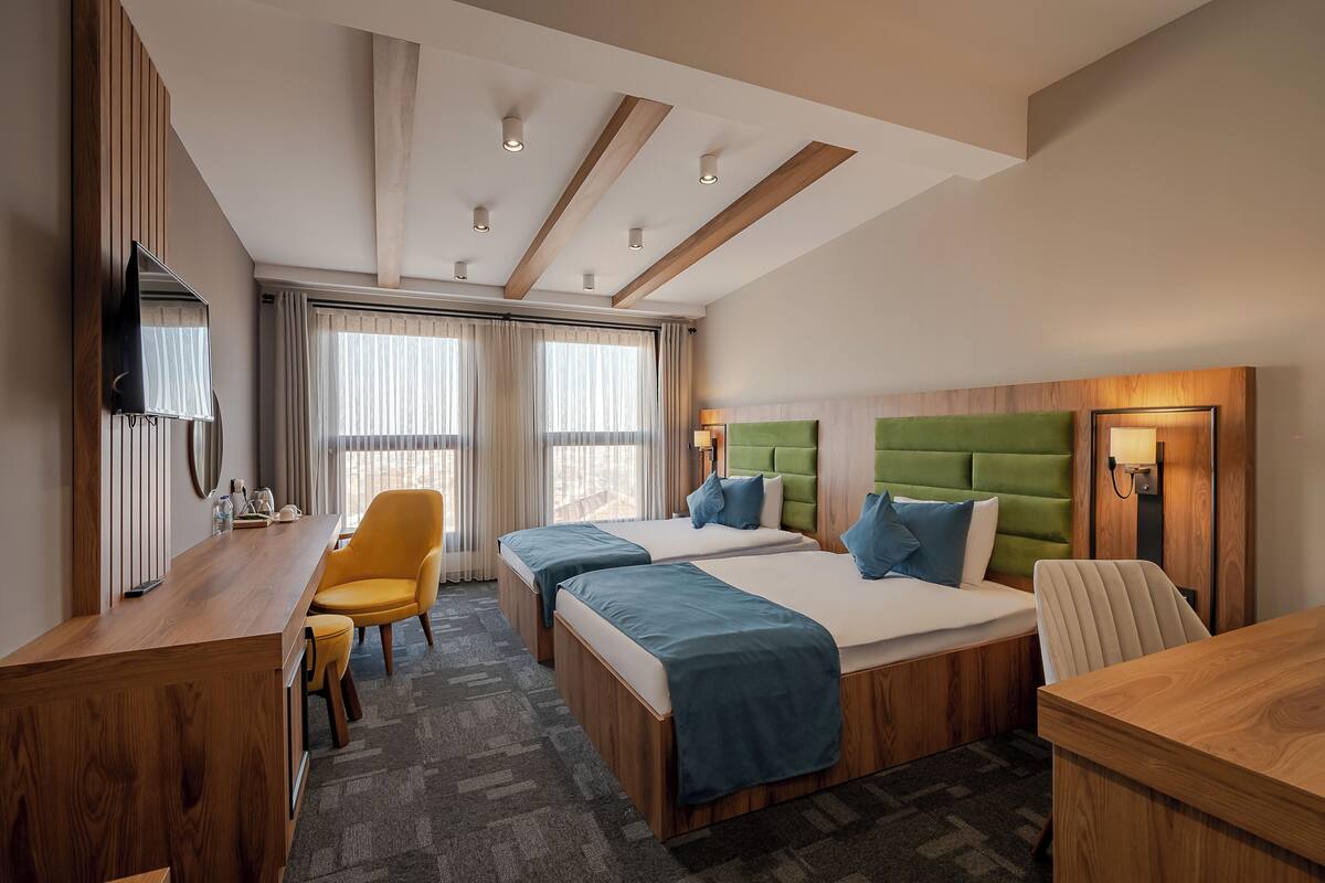 A hotel room with two beds, a desk, a chair, a TV, and a window with curtains.