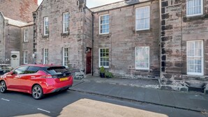 A red car parked in front of a stone building with multiple windows and a door. - 2 bedroom accommodation in Berwick Upon Tweed (Berwick Upon Tweed)