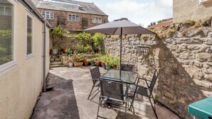 A patio with a table and chairs, surrounded by potted plants and a stone wall. - 2 bedroom accommodation in Berwick Upon Tweed (Berwick Upon Tweed)