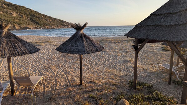 Une plage avec des parasols en chaume, une structure en bois et une chaise.