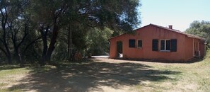 Une maison rustique, accessible par un chemin de terre, et entourée d’arbres.