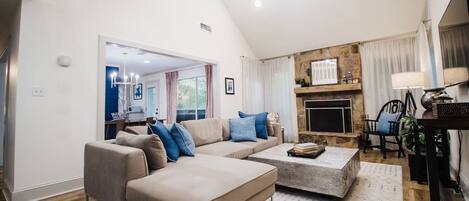 Uma sala de estar espaçosa com um amplo sofá modular, lareira e um espaço de jantar com mesa e cadeiras.