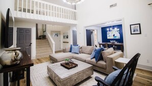 A spacious living room with a high ceiling, a staircase, a dining area, and a kitchen visible through an open door. - Stunning Lake House 4Bdm w/ Sandy Beach Access (Pottsboro)