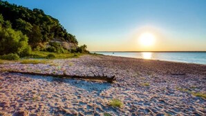 A beach with a wooden structure in the foreground and a forested cliff in the background. - Stunning Lake House 4Bdm w/ Sandy Beach Access (Pottsboro)