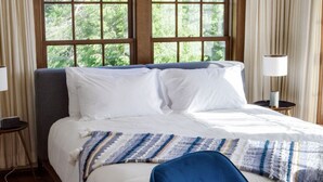 A bedroom with a bed, a blue chair, a bedside table with a lamp, and a window with curtains.