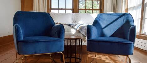 Une pièce avec deux fauteuils bleus, une petite table ronde et un lit recouvert de linge de maison blanc.