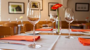 A dining area with tables set for a meal, featuring wine glasses and orange napkins.