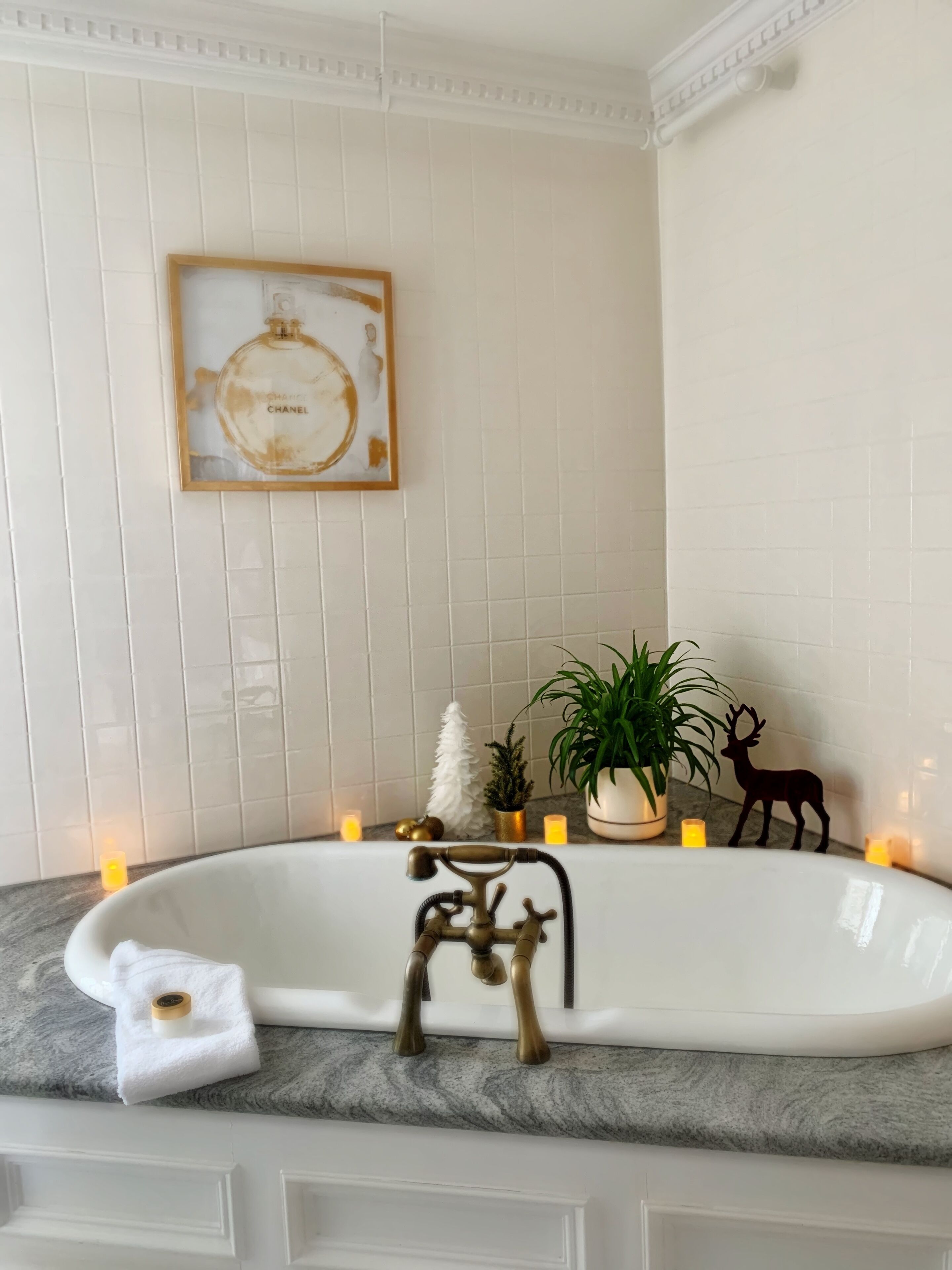 Un baño con una bañera blanca, un cuadro en la pared y elementos decorativos como velas y una planta.