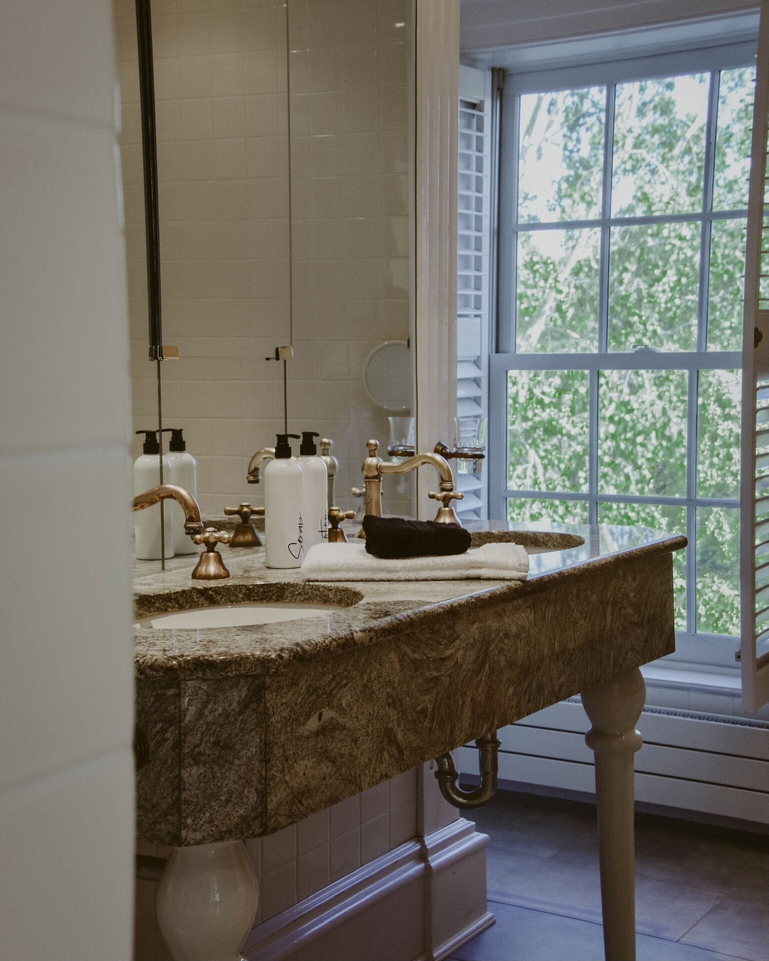 A bathroom with a marble sink, a large mirror, and a window with a view of trees.
