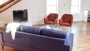 A living room with a blue sofa, two red armchairs, a glass coffee table, and a TV on a white stand.