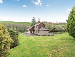 Une maison en pierre avec un toit rouge, un petit abri attenant et une pelouse bien entretenue.