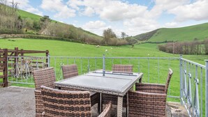 An outdoor seating area with wicker furniture and a table, overlooking a green field with sheep. - Lovely detached property in a rural location on the Welsh border. (Llanfihangel Nant Melan, near Presteigne)