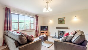 A living room with two leather sofas, a television, a fireplace, and a large window with curtains. - Lovely detached property in a rural location on the Welsh border. (Llanfihangel Nant Melan, near Presteigne)