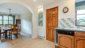 A kitchen with wooden cabinets, a built-in dishwasher, and a dining area with a table and chairs. - Lovely detached property in a rural location on the Welsh border. (Llanfihangel Nant Melan, near Presteigne)